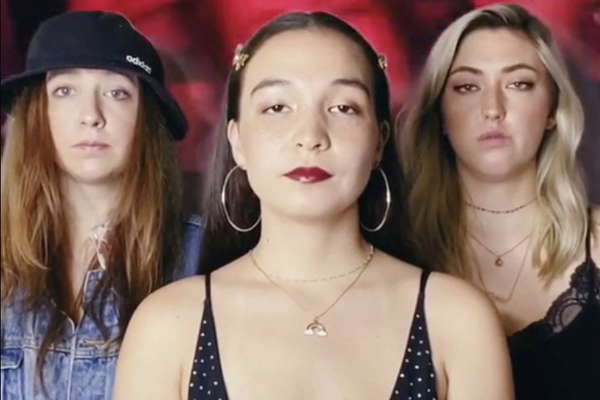 Three young women posing confidently in a music video setting.